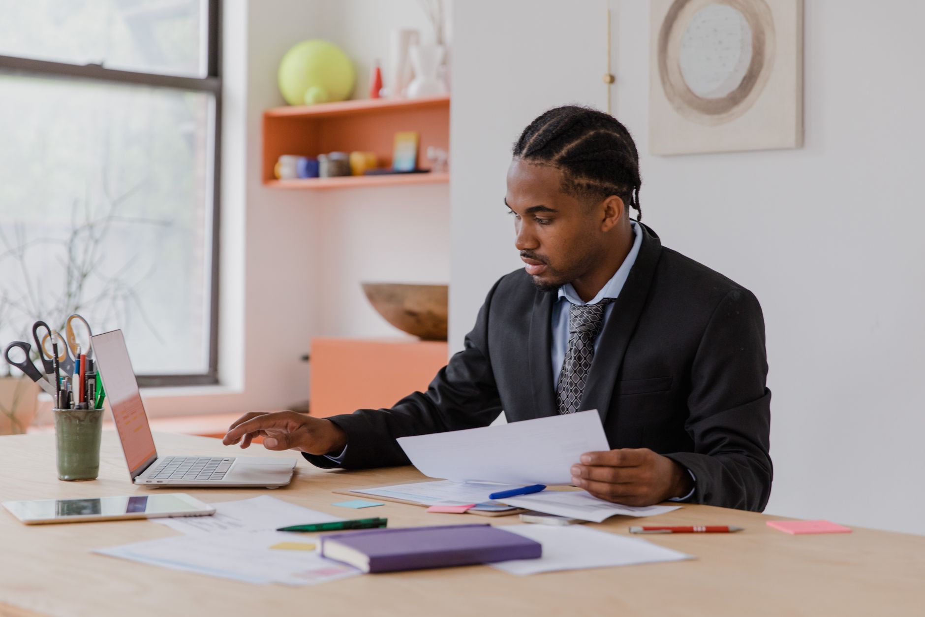 A focused person reviewing documents and a laptop screen at a desk in a home office