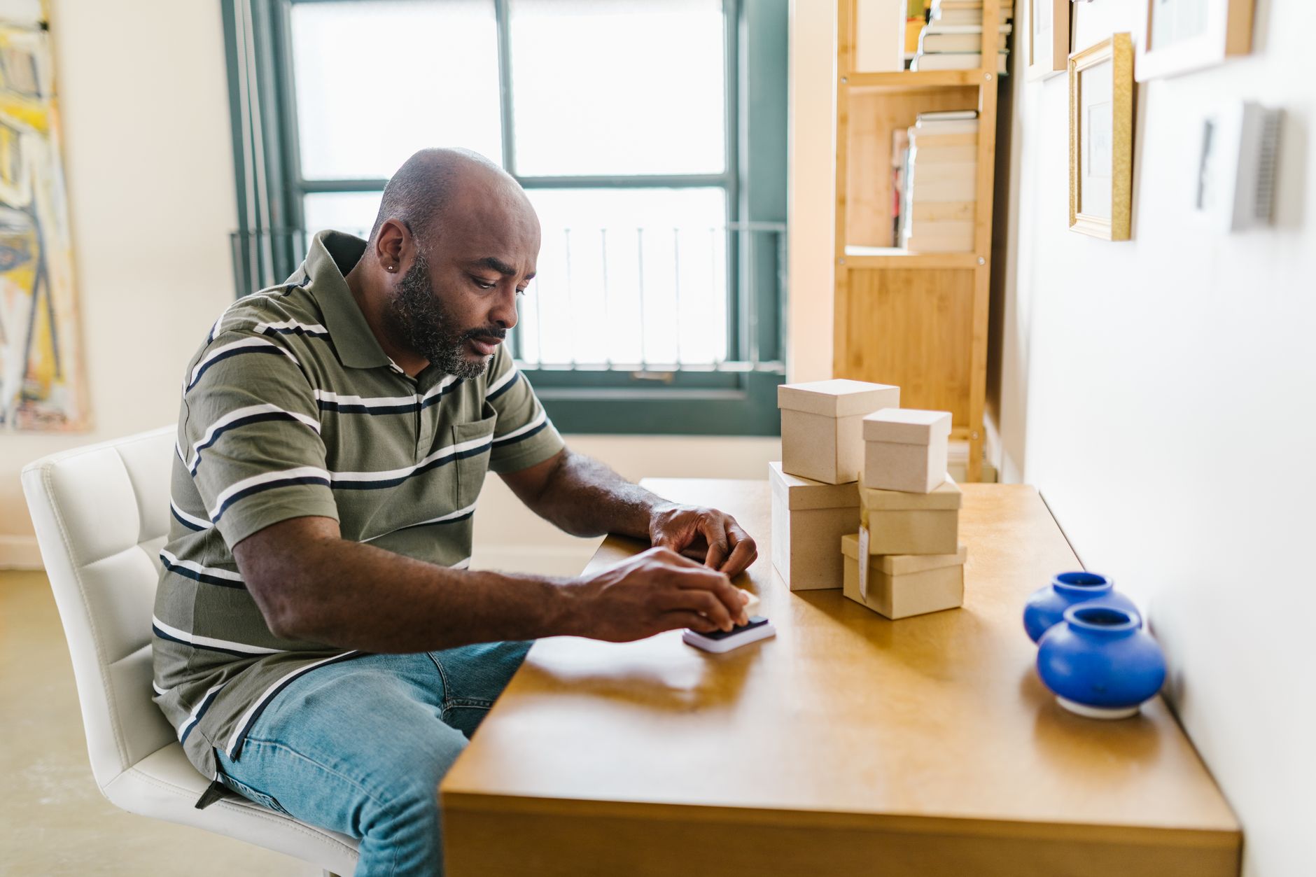 A person at a home desk preparing a small business project, packages and laptop nearby